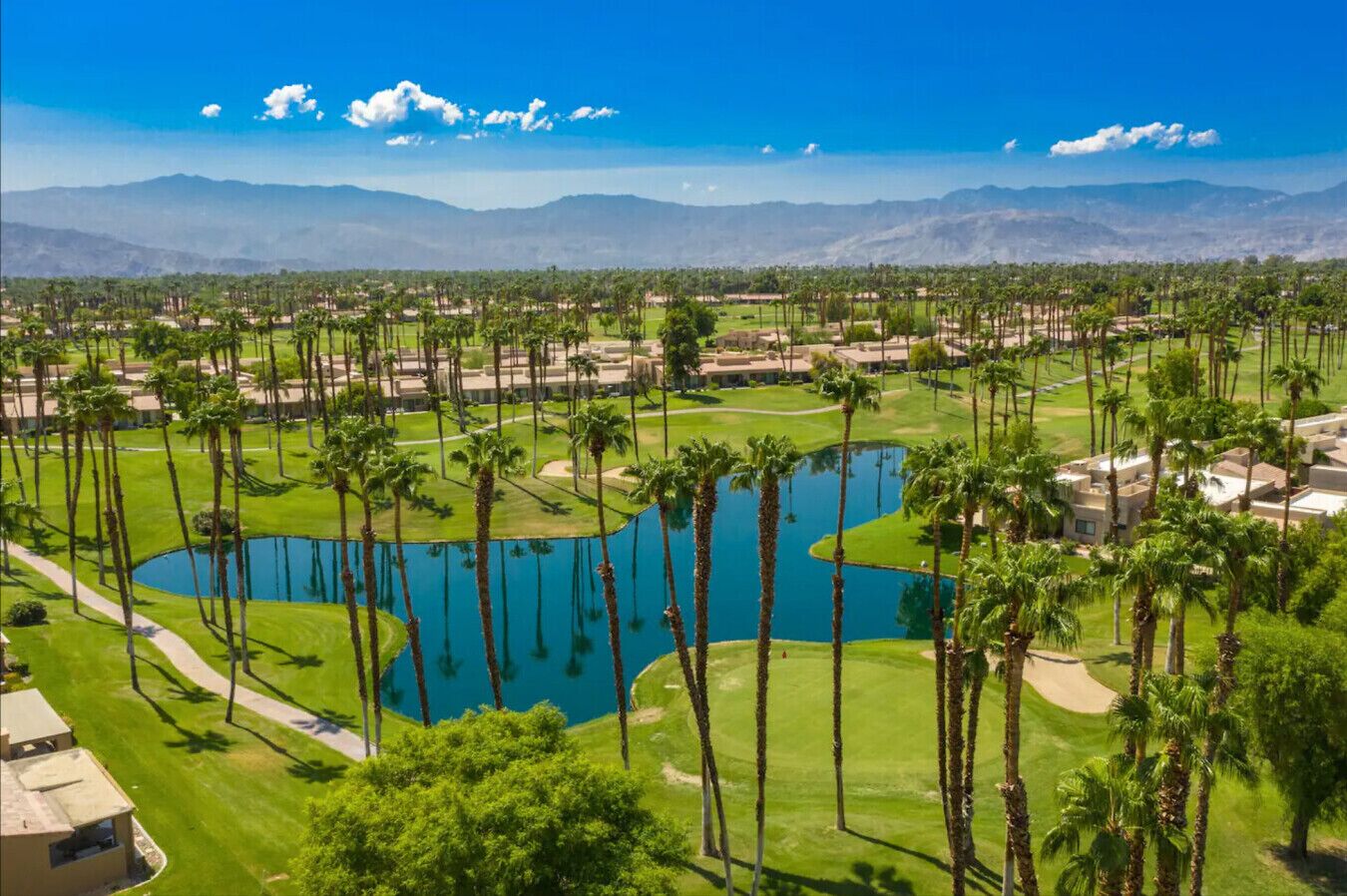 A golf course with multiple ponds, palm trees, and a mountainous backdrop.