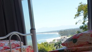 Ein Bett mit floraler Bettwäsche und Blick auf das Meer durch große Fenster.