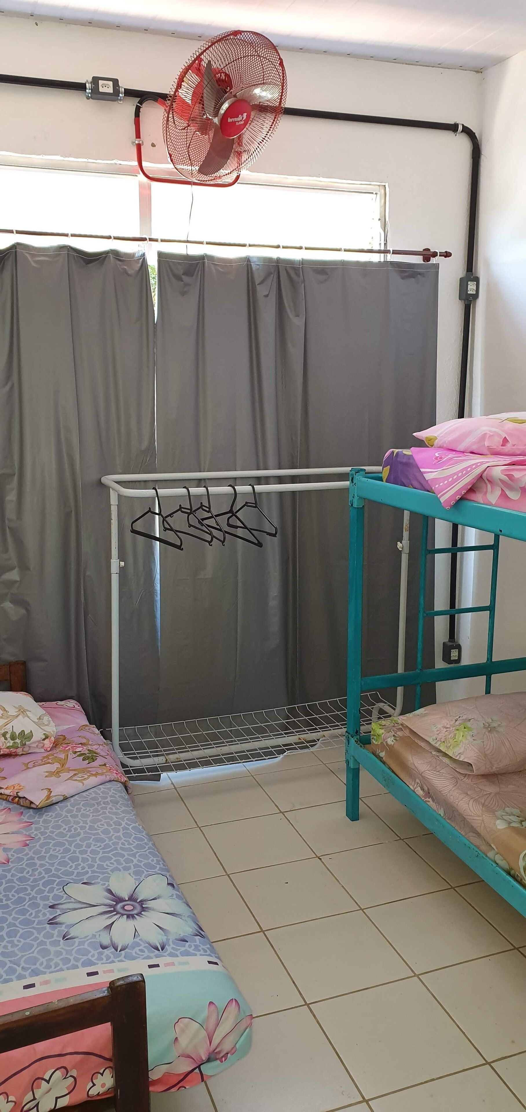 Quarto com cama, ventilador, varal e mesa com toalha de mesa florida.