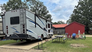 A recreational vehicle (RV) parked in a grassy area with picnic tables and chairs nearby. - Spacious RV in Brilliant Broken Bow with AC, WiFi, near Day Spa and Winery! (Broken Bow)