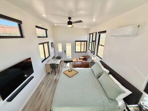 A compact, well-lit room with a bed, seating area, and a TV. - Journey Pines: Secluded Tiny Home w/ Hot Tub (Kanab)