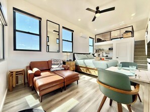 A modern apartment with a loft-style kitchen, a sofa, a dining table, and a chair.