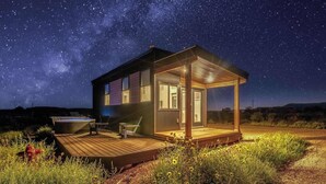 A cabin with a wooden deck, a hot tub, and a starry night sky. - Journey Pines: Secluded Tiny Home w/ Hot Tub (Kanab)