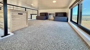 A spacious room with a high ceiling, a large window offering a view, and a carpeted floor. - Journey Pines: Secluded Tiny Home w/ Hot Tub (Kanab)