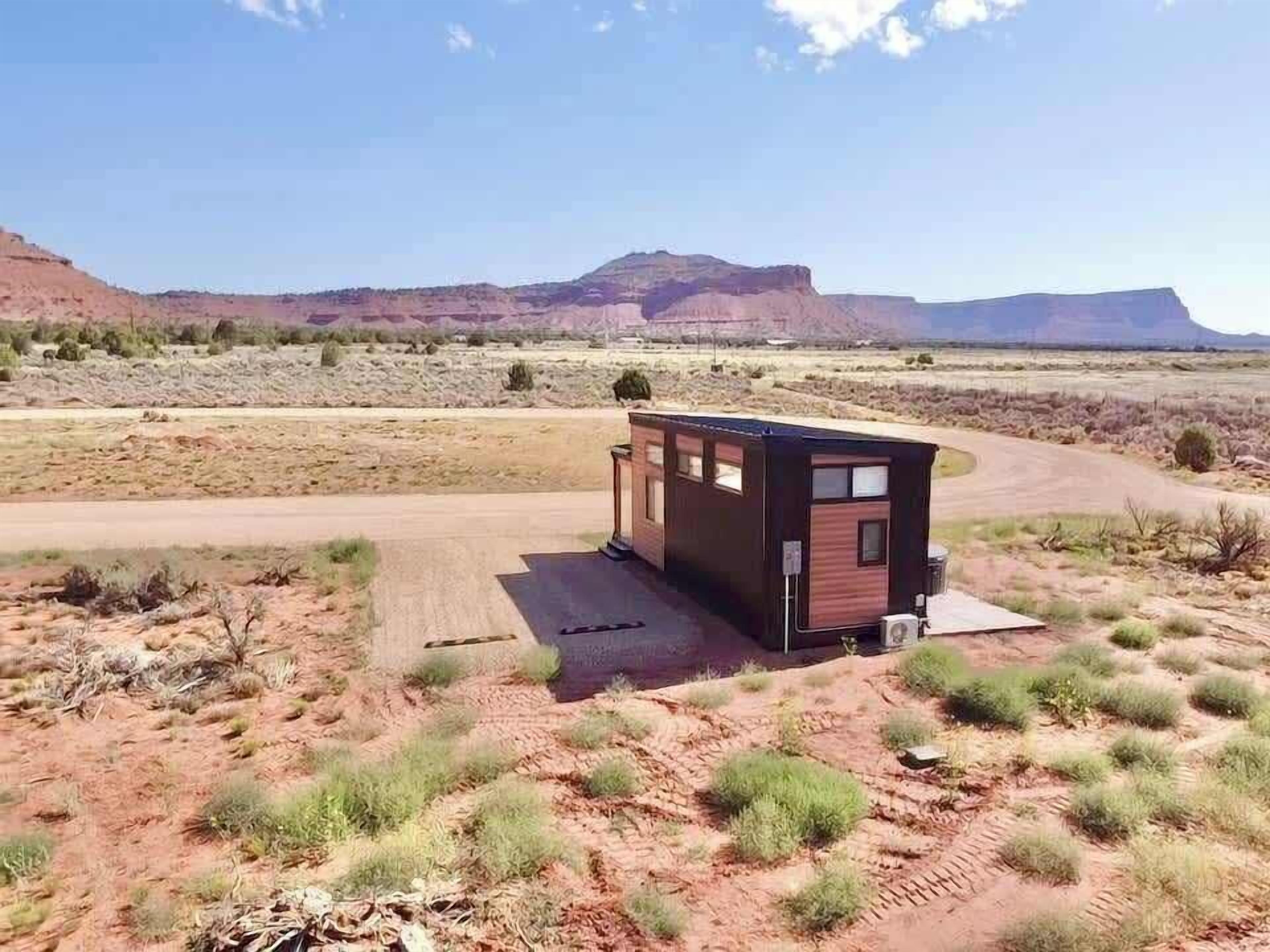 A small, modern cabin with a flat roof, situated in a desert landscape with distant mountains.