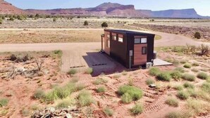 A small, modern cabin with a flat roof, situated in a desert landscape with distant mountains. - Journey Pines: Secluded Tiny Home w/ Hot Tub (Kanab)