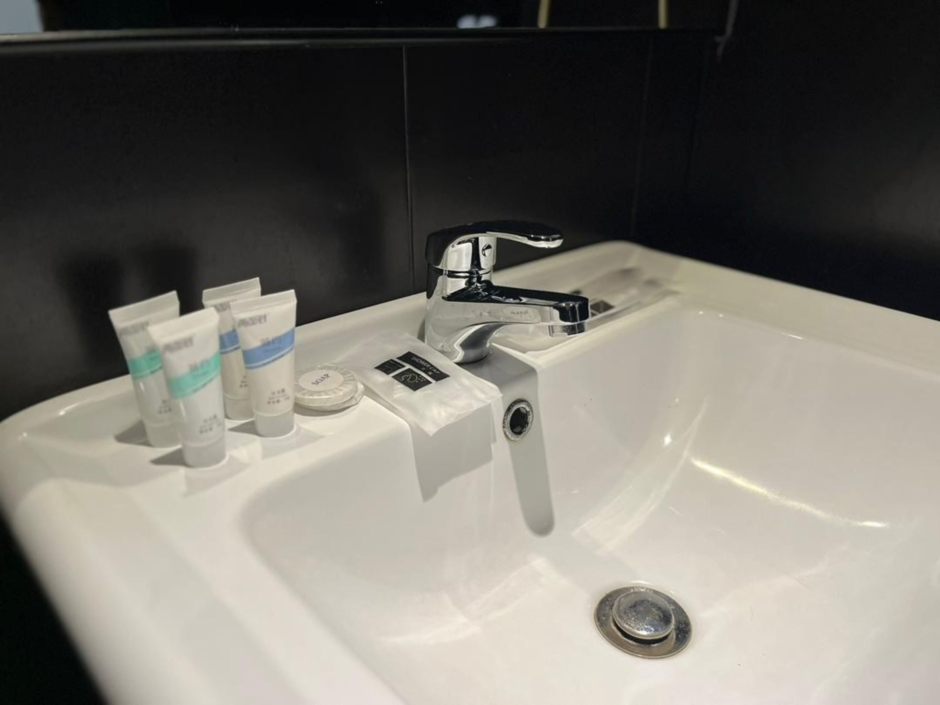 A white bathroom sink with a modern faucet, a soap dispenser, and two tubes of hand soap.