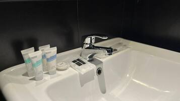 A white bathroom sink with a modern faucet, a soap dispenser, and two tubes of hand soap.