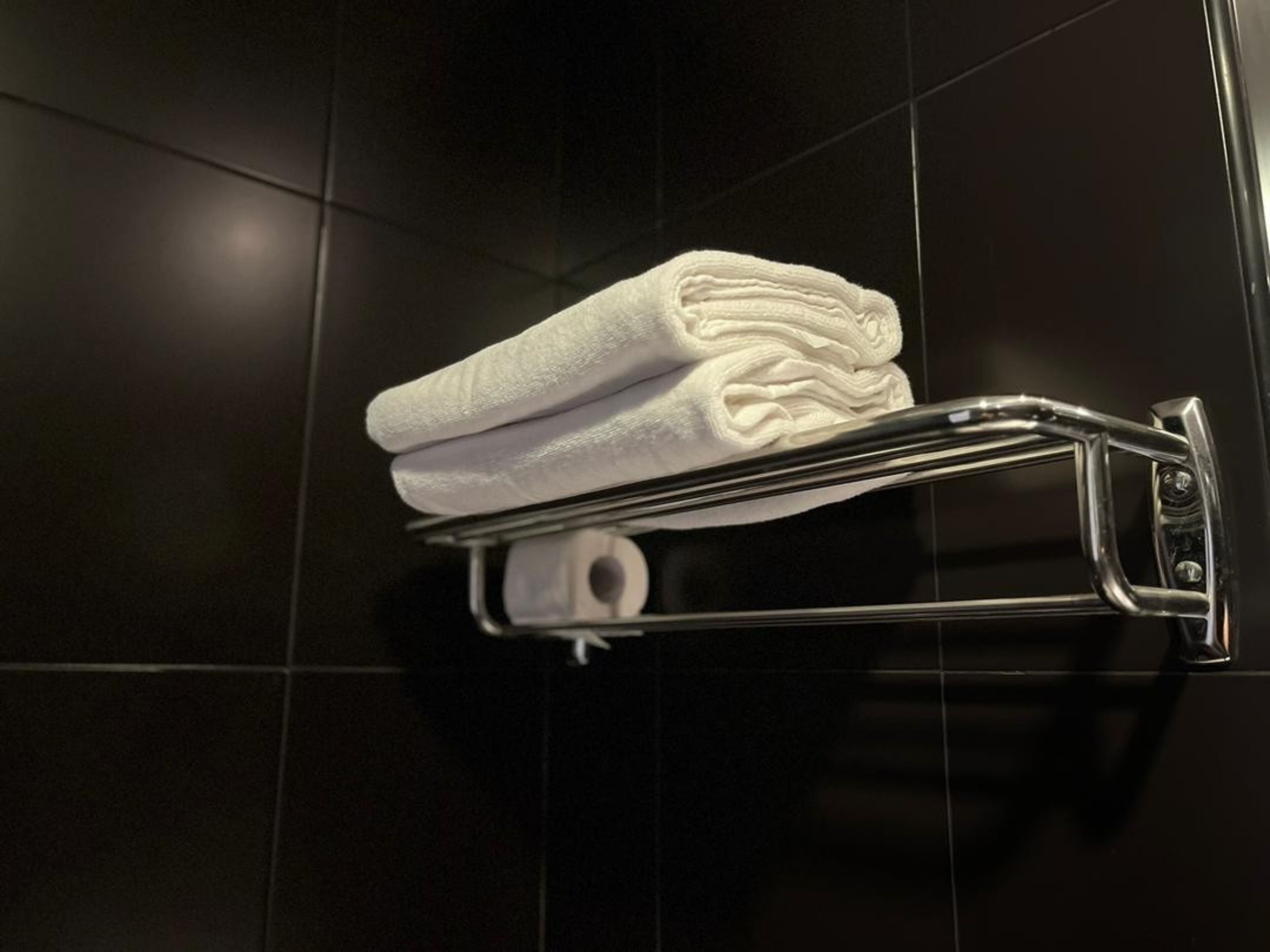 A folded white towel on a metallic towel rack in a tiled room.