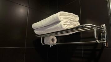 A folded white towel on a metallic towel rack in a tiled room.
