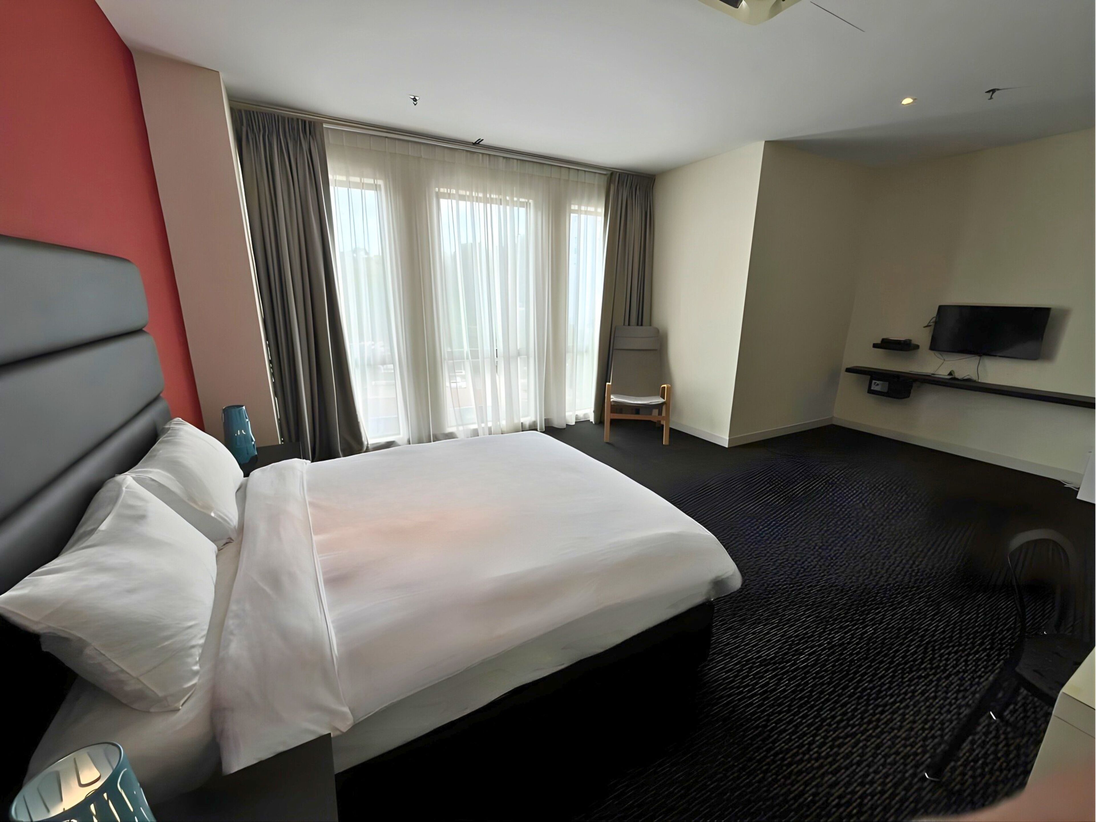 A hotel room with a large bed, a chair, a TV, and a window with curtains.