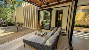 Un espace extérieur moderne aménagé avec un canapé et une table, une sculpture de cactus et une vue sur une piscine, visible à travers une porte vitrée.
