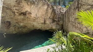 Une grotte naturelle, avec de l’eau claire, entourée de végétation et dotée d’une terrasse en bois.