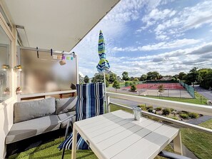 A balcony with a sofa, a table, and a view of a sports court.