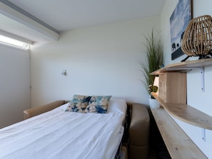 Une chambre à coucher comprenant un lit, une chaise, une table de chevet, une étagère fixée au mur et une plante en pot.