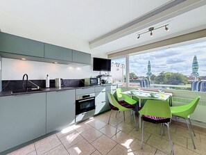 Une cuisine moderne avec un coin repas, de grandes fenêtres et une vue sur un bâtiment situé au loin.