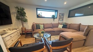 Ein Wohnzimmer mit Ecksofa, Couchtisch, Fernseher, Pflanze und einem Fenster.