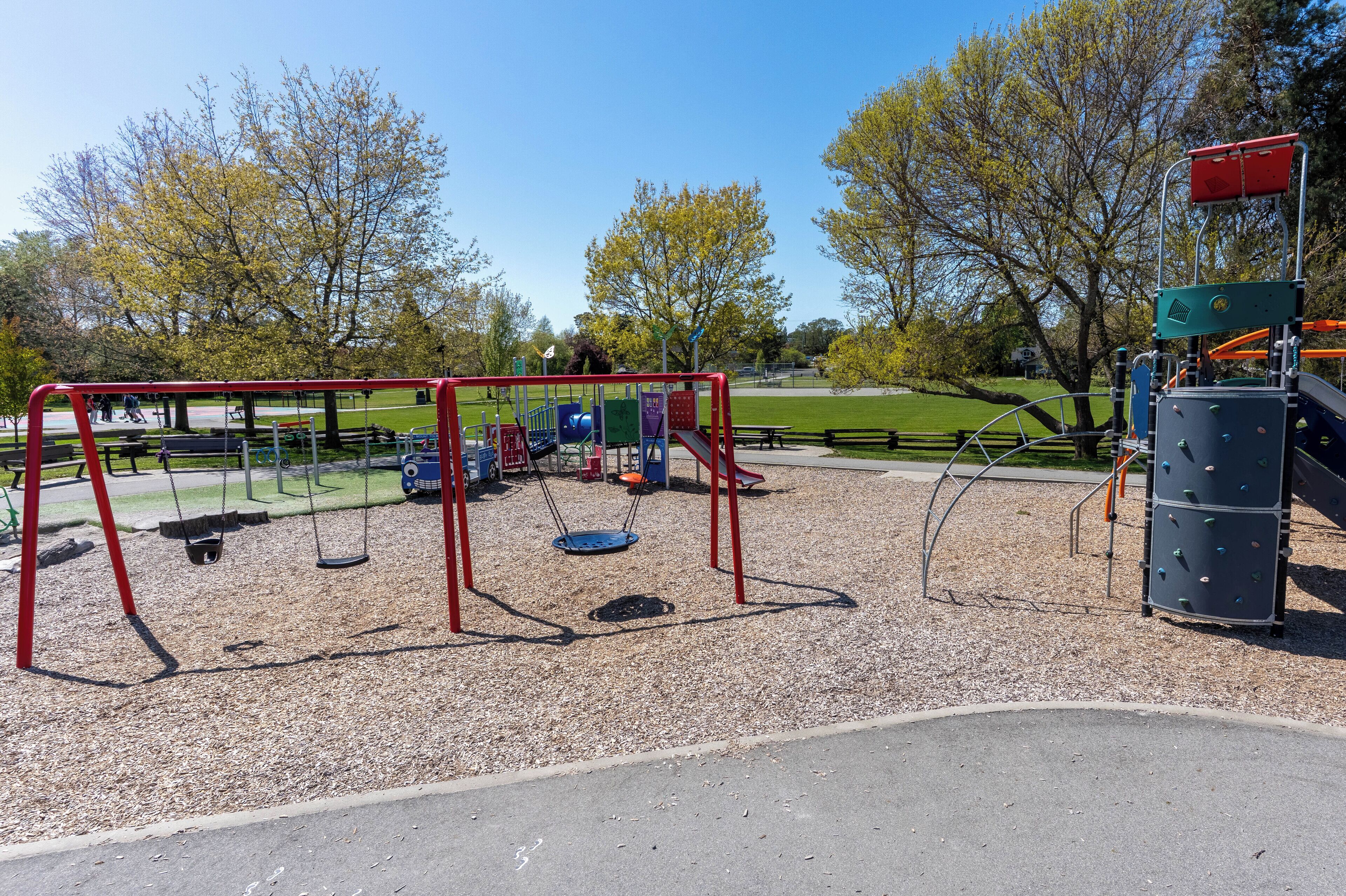 Un parc infantil amb cadira de balanceig, elements per escalar i una zona tancada per taronja.