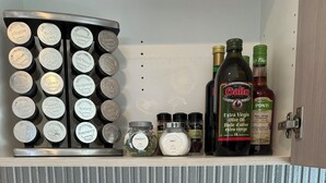 Eine Küche mit einer Gewürzregal, Gläsern mit Gewürzen, Olivenölflaschen und Holzkochlöffeln.