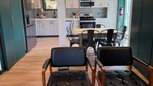 Eine moderne Küche mit Edelstahlgeräten, ein Essbereich mit Holztisch und schwarzen Stühlen sowie ein Ausblick ins Freie durch ein Fenster.
