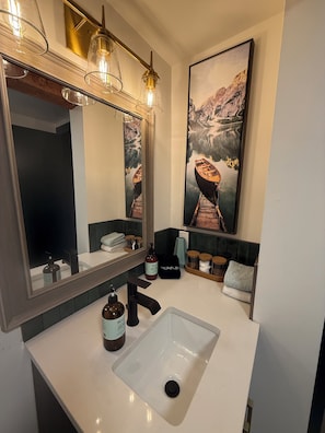 Un baño moderno con un espejo grande, un lavabo blanco y un cuadro de un barco en un lago.