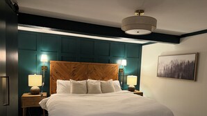 Ein ordentlich bezogenes Bett mit zwei Nachttischlampen, einem Kopfteil mit Fischgrätmuster und einem Bild an der Wand.