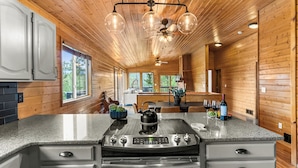 Una cocina moderna con paredes de madera, encimera de granito, estufa de acero inoxidable y ventilador de techo con luces.