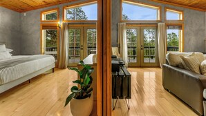 Una habitación amplia con cama, sofá, escritorio y un ventanal con vistas a árboles.