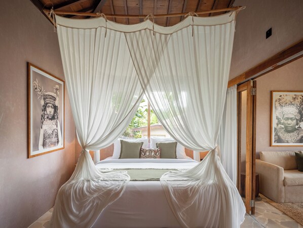Ein Schlafzimmer mit Himmelbett, gerahmten Kunstwerken an den Wänden und Blick auf Grünflächen.