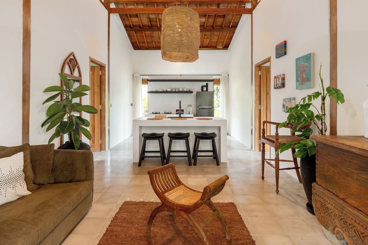 Un vaste espace de vie doté d’un plafond en bois, d’un canapé, d’un fauteuil et d’une table à manger avec des chaises.