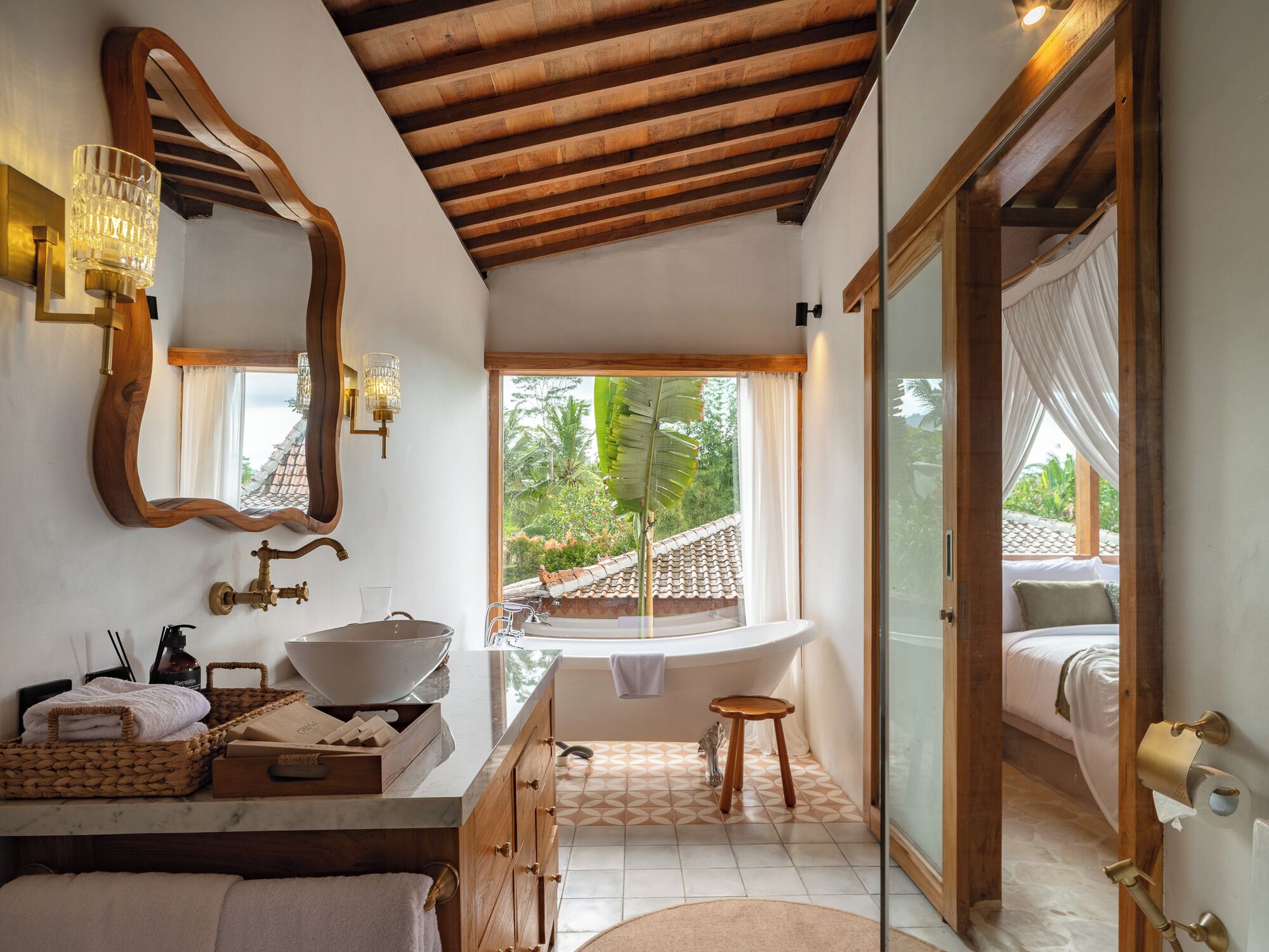Un baño con un espejo grande, un lavamanos, una bañera y una ventana con vistas al tejado y la vegetación.