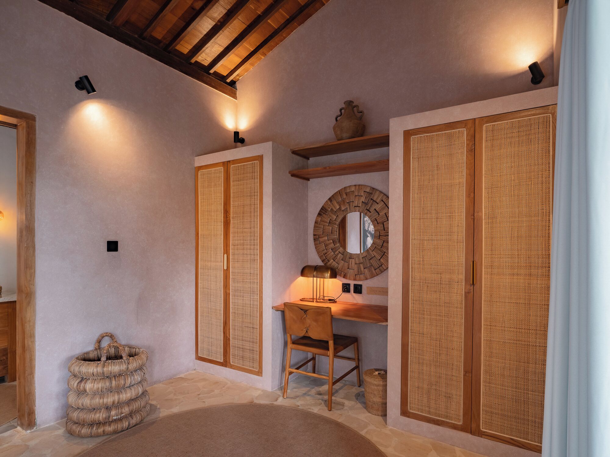 Une pièce avec un bureau en bois, une chaise, un panier en osier et un miroir rond accroché au mur.