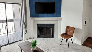 Una sala de estar con chimenea, un televisor montado encima y puertas corredizas de vidrio, además de una silla marrón.