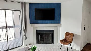 A living room with a fireplace, a television mounted above it, a sliding glass door, and a brown chair.