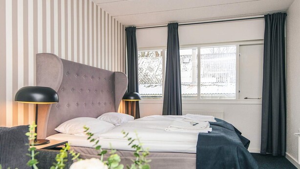 A hotel room with a bed, two bedside lamps, a window with curtains, and a view of the outside. - 4 Person Holiday Park Home in Give (Give)