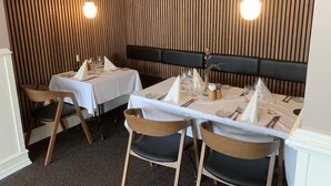 A restaurant with two tables set for dining, each with white tablecloths, wooden chairs, and a black upholstered headboard. - 4 Person Holiday Park Home in Give (Give)