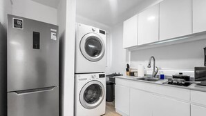 A compact kitchen with a stainless steel refrigerator, a double-door washer and dryer, a sink, and a stove. - Casa Canova | Duplex Full Home For 14PPL @San Juan (San Juan)