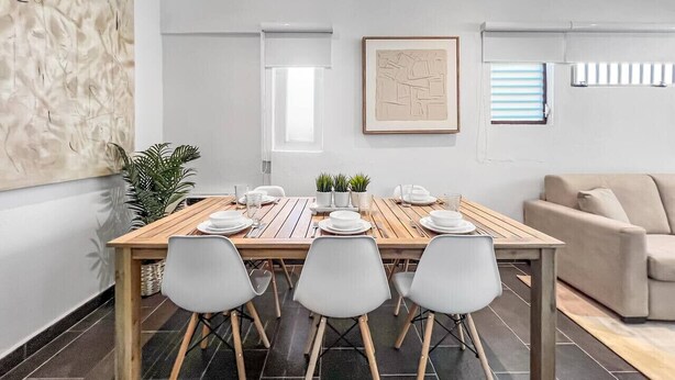 A dining area with a wooden table set for four, white chairs, and a beige sofa in the background. - Casa Canova | Duplex Full Home For 14PPL @San Juan (San Juan)