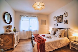 A bedroom with a bed, a dresser, a mirror, a window with curtains, and wall decorations.