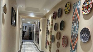 A hallway with patterned floor tiles, a series of wall-mounted decorative plates, and a framed picture on the left wall. - al Madina Hotel Samarkand  (Samarkand)