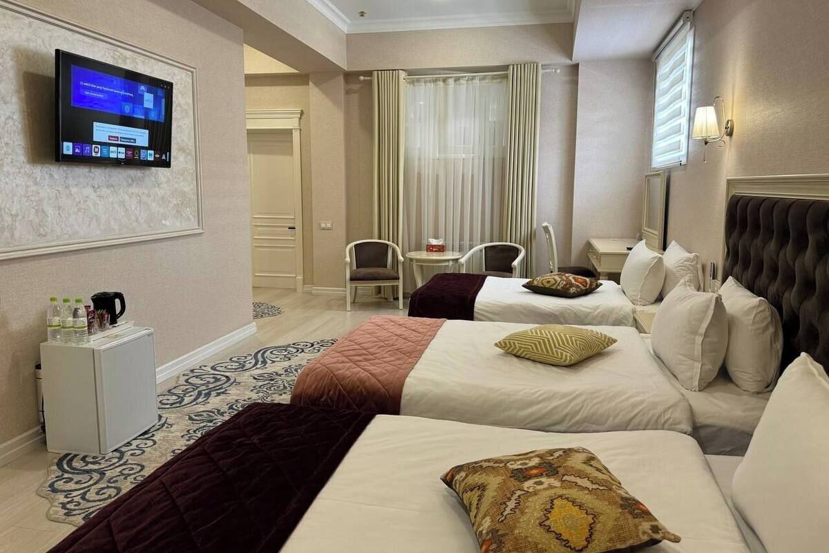 A hotel room with two beds, a TV mounted on the wall, a small fridge, and a seating area with chairs and a table.