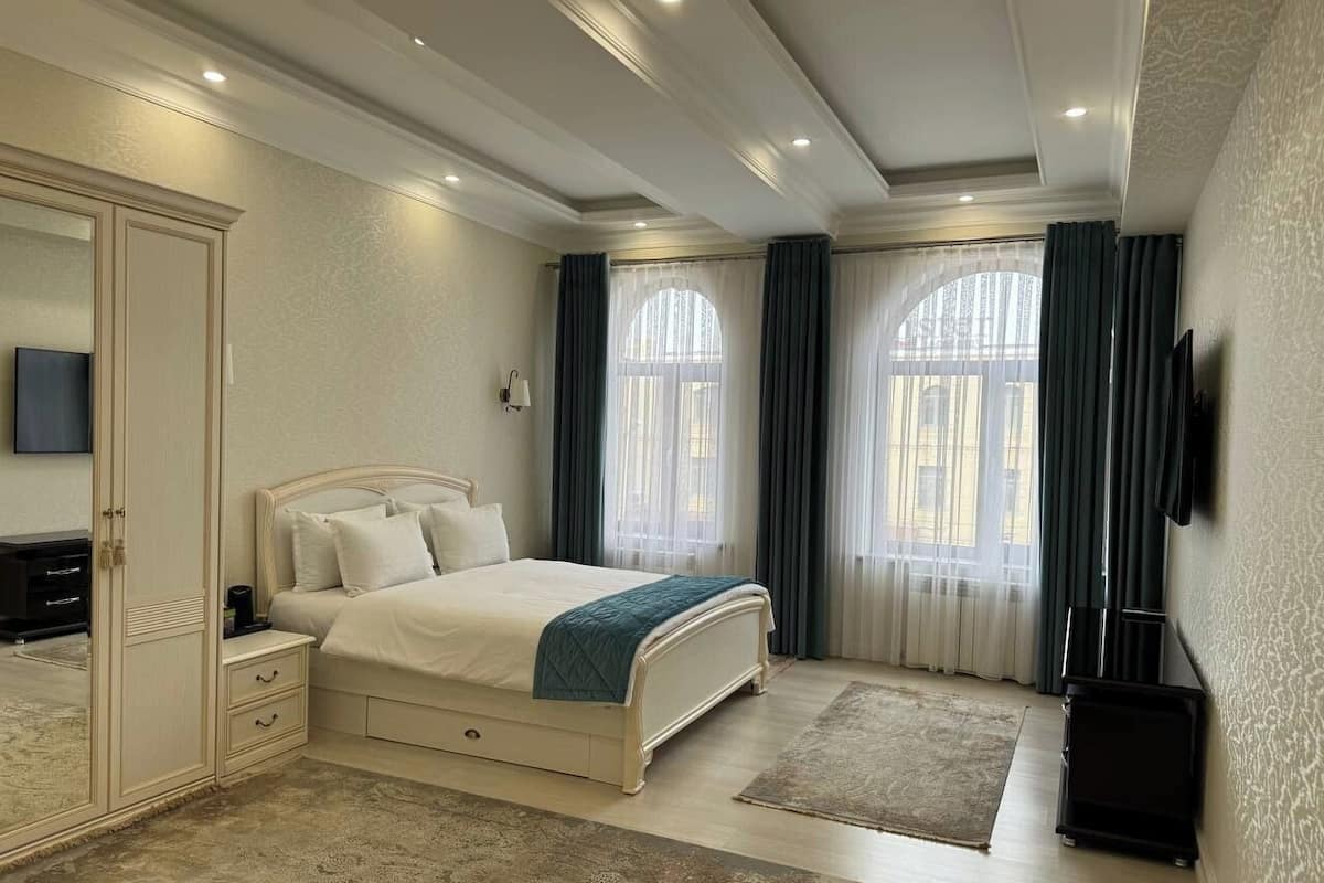 A bedroom with a bed, nightstands, a wardrobe, a television, and a large window with curtains.