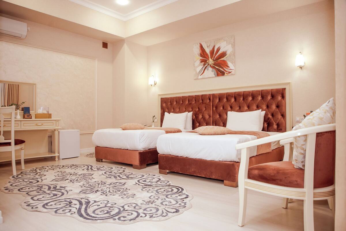 A hotel room with two beds, a desk, a chair, and a decorative rug.
