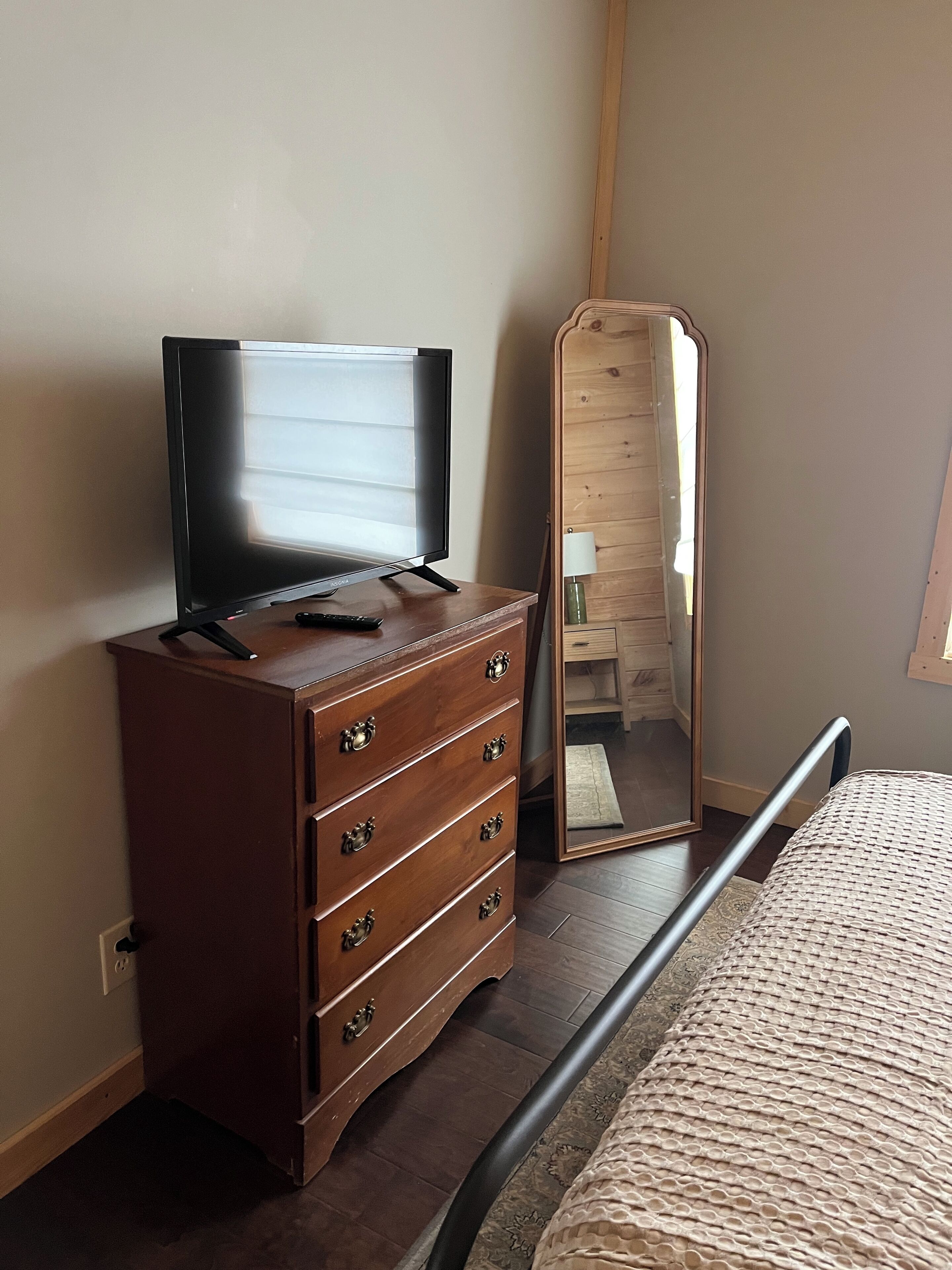 Un dormitorio con un aparador de madera, un televisor, un espejo y una cama con colcha estampada.