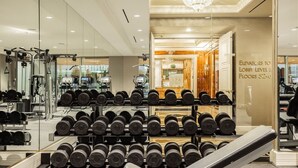 A gym with various exercise equipment, a rack of dumbbells, and a sign indicating elevators to lobby level and floors 52-56.