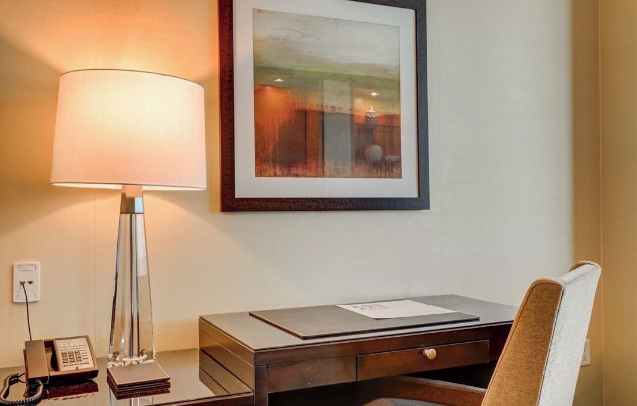 Une chambre d’hôtel équipée d’un bureau, d’une lampe, d’un tableau encadré au mur et d’un téléphone.
