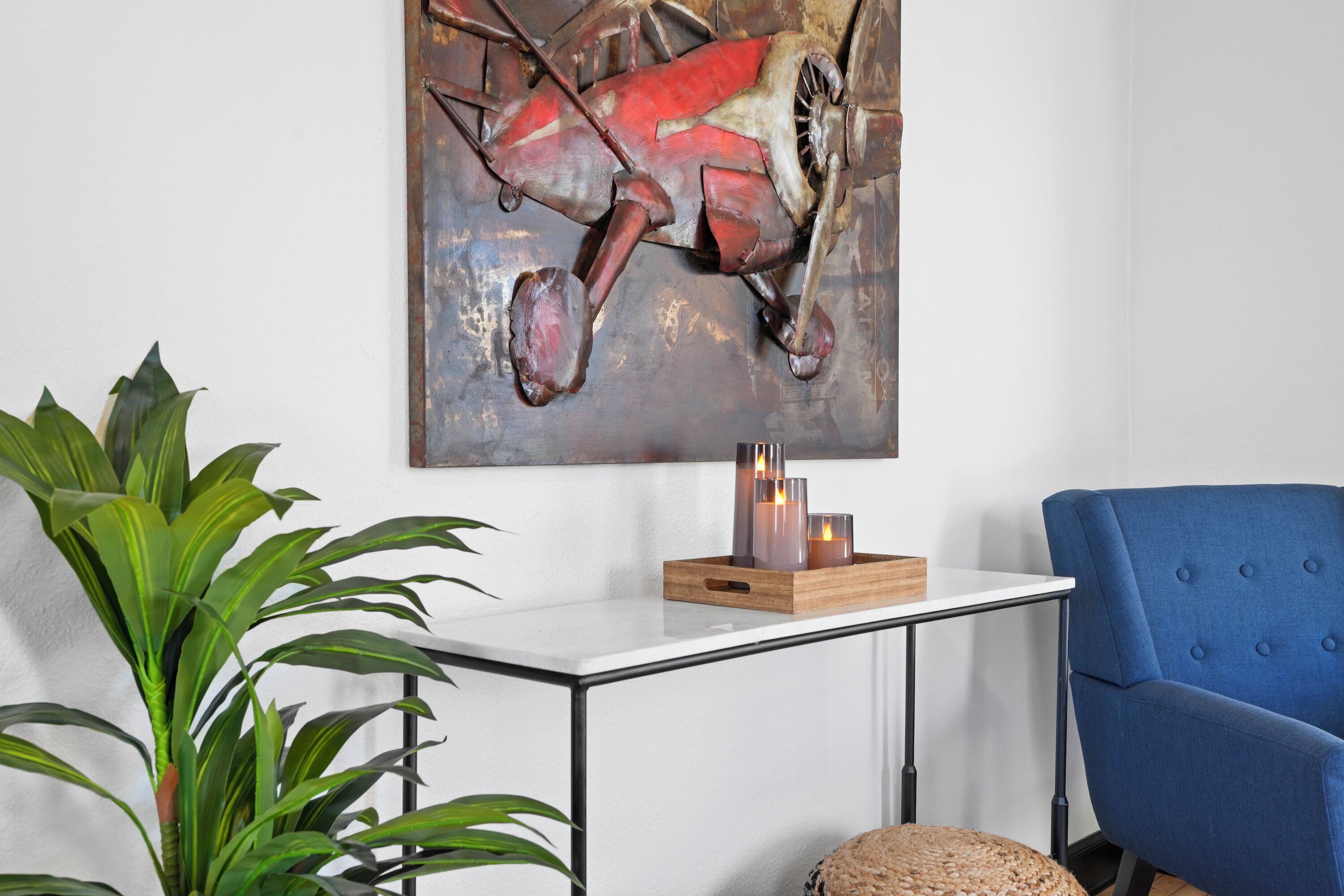 A modern living room with a white table, a blue armchair, a large abstract painting, and a potted plant.
