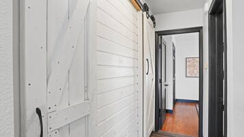 A hallway with a white door and a black door leading to a room with a wooden floor.