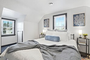 A neatly arranged bedroom with a large bed, two bedside tables with lamps, and two wall-mounted artworks.