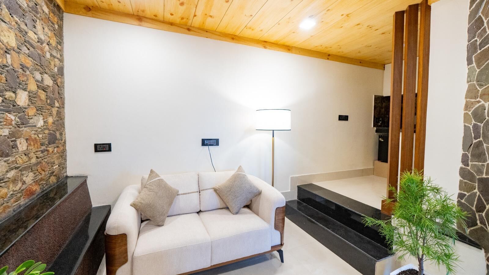 A modern living room with a stone wall, a white sofa with cushions, a floor lamp, and a staircase leading to another level.